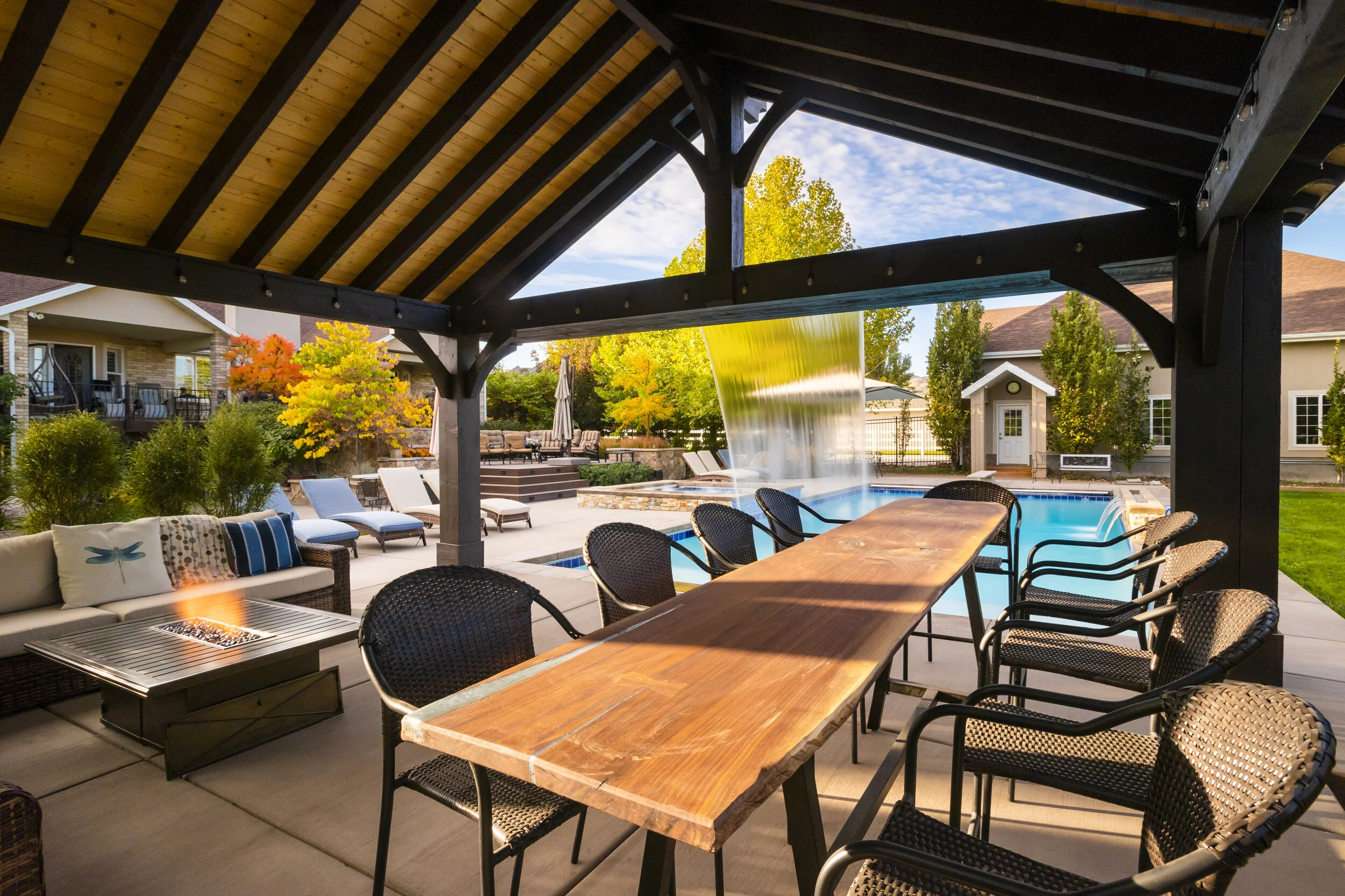 A covered outdoor living space features a long wooden bar table