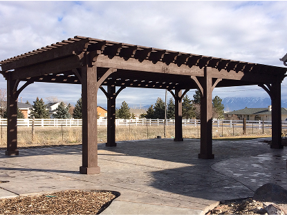 A long, rectangular, dark-stained wooden pergola stands on a stamped concrete patio