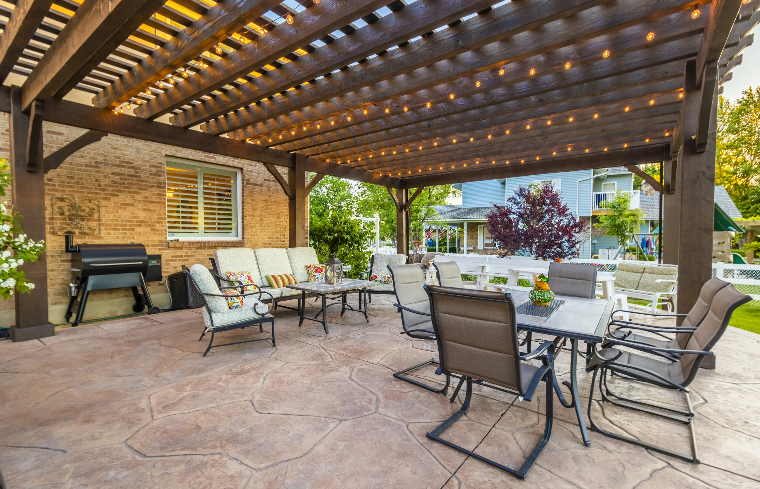 A wide view of a spacious outdoor patio features a large dark-stained pergola