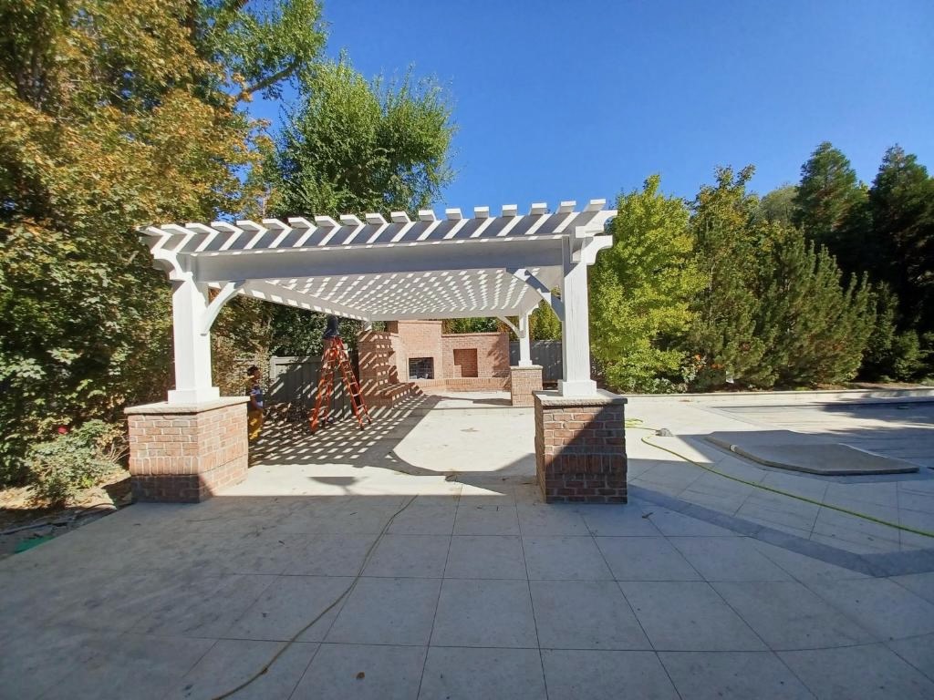 Free Standing Patio Pergola With Brick Columns Large free standing patio pergola with white timber beams and brick columns providing shade over an outdoor fireplace area