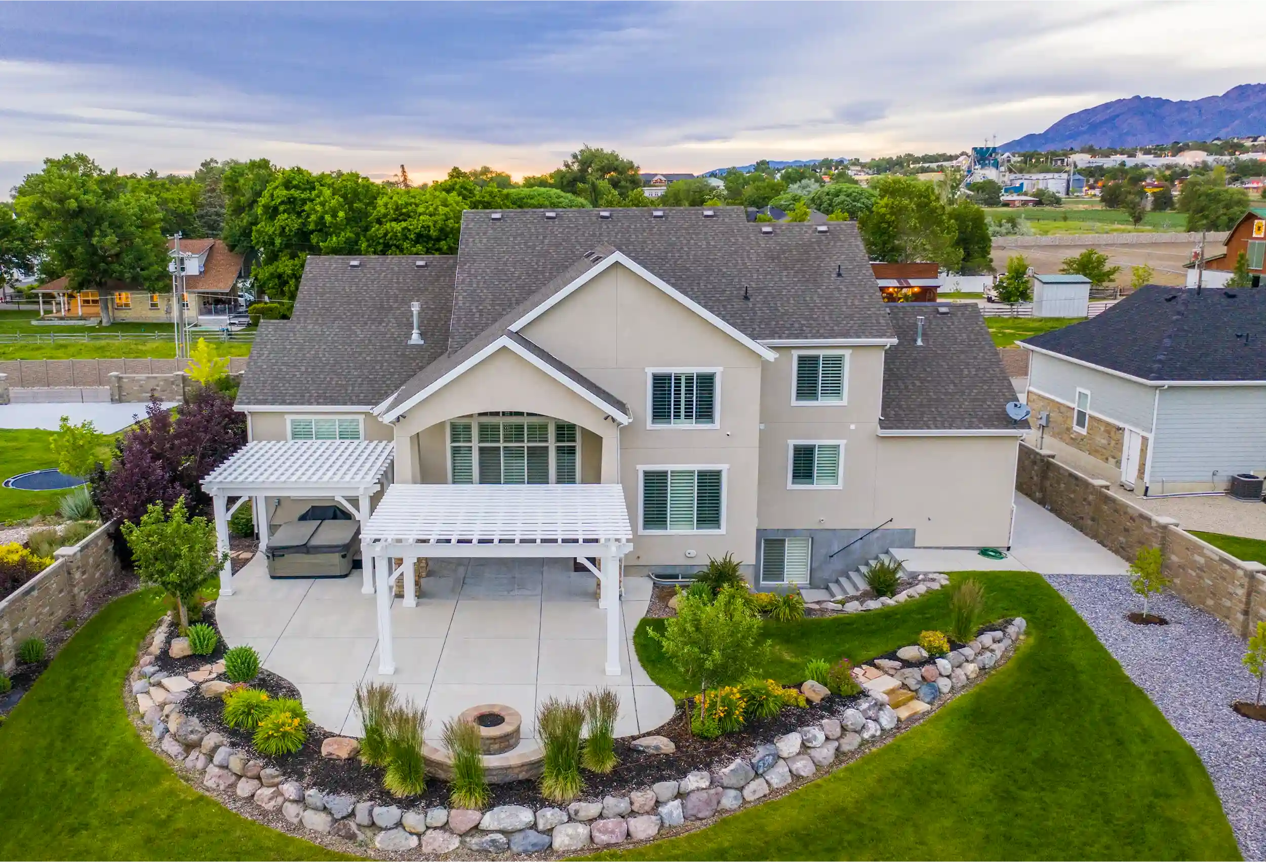 Backyard with Dual Timber Frame Pergolas Overhead view of a home patio with a Timber frame pergola and side pergola, landscaped garden, fire pit, and lush lawn