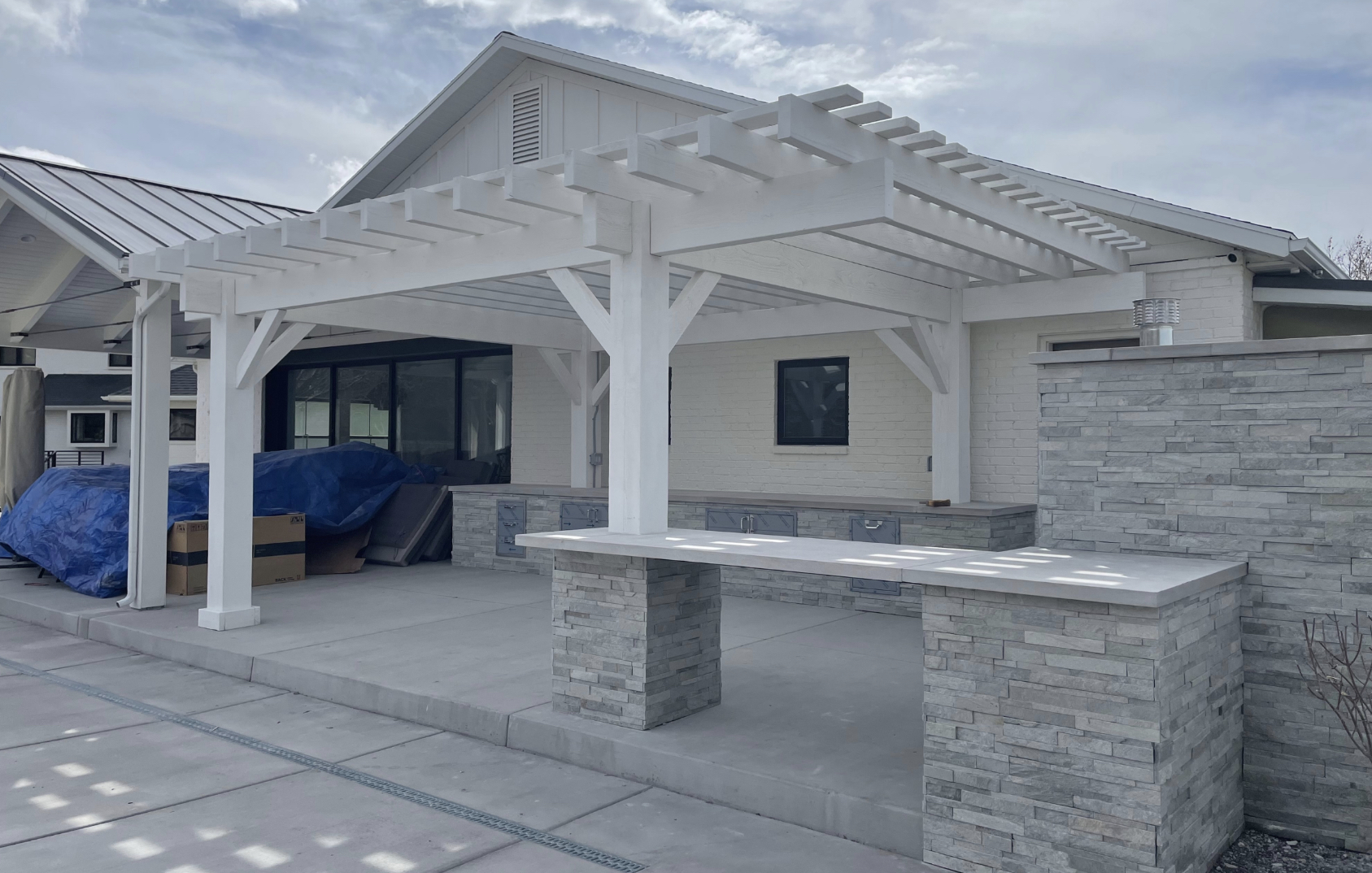 White Pergola with Stone Bar and Patio Kitchen White timber pergola over patio with stone bar and cabinets, creating a bright, shaded outdoor living space for dining.
