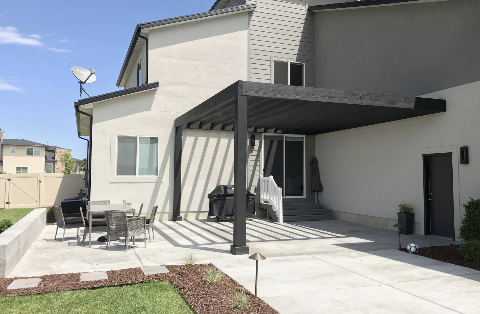 Modern Attached Pergola Over Backyard Patio Modern attached pergola casts striped shade over a concrete patio with seating and grill, creating a functional outdoor living space.