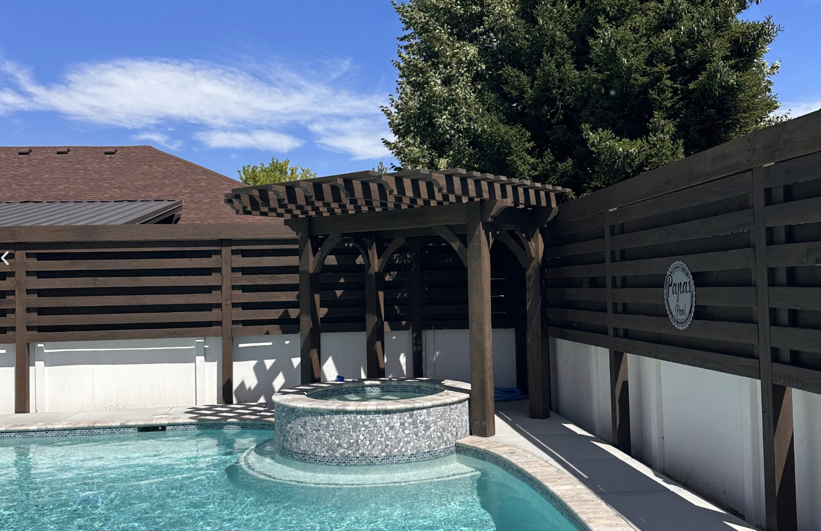 Poolside Backyard Pergola with Spa Shade Poolside backyard pergola shading a raised spa beside a privacy fence; dark timber frame adds style and cooling shade