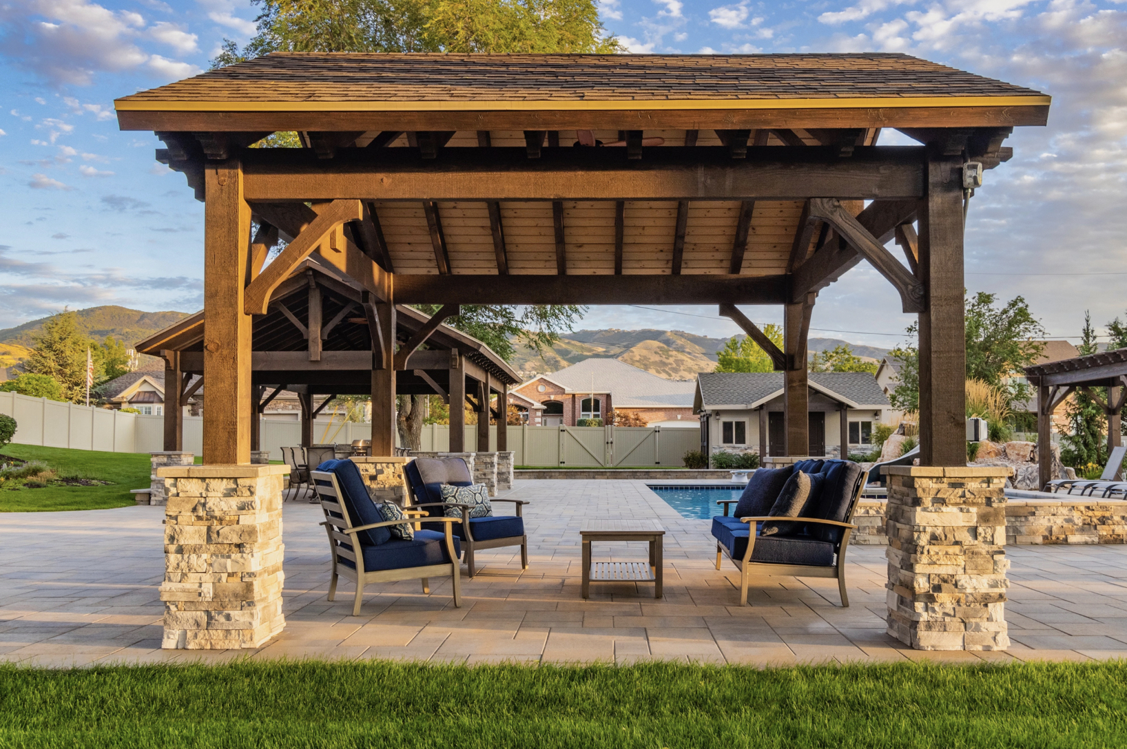 Timber-frame pavilion with posts and lounge seating by a pool, showcasing garden pavilions for refined outdoor living