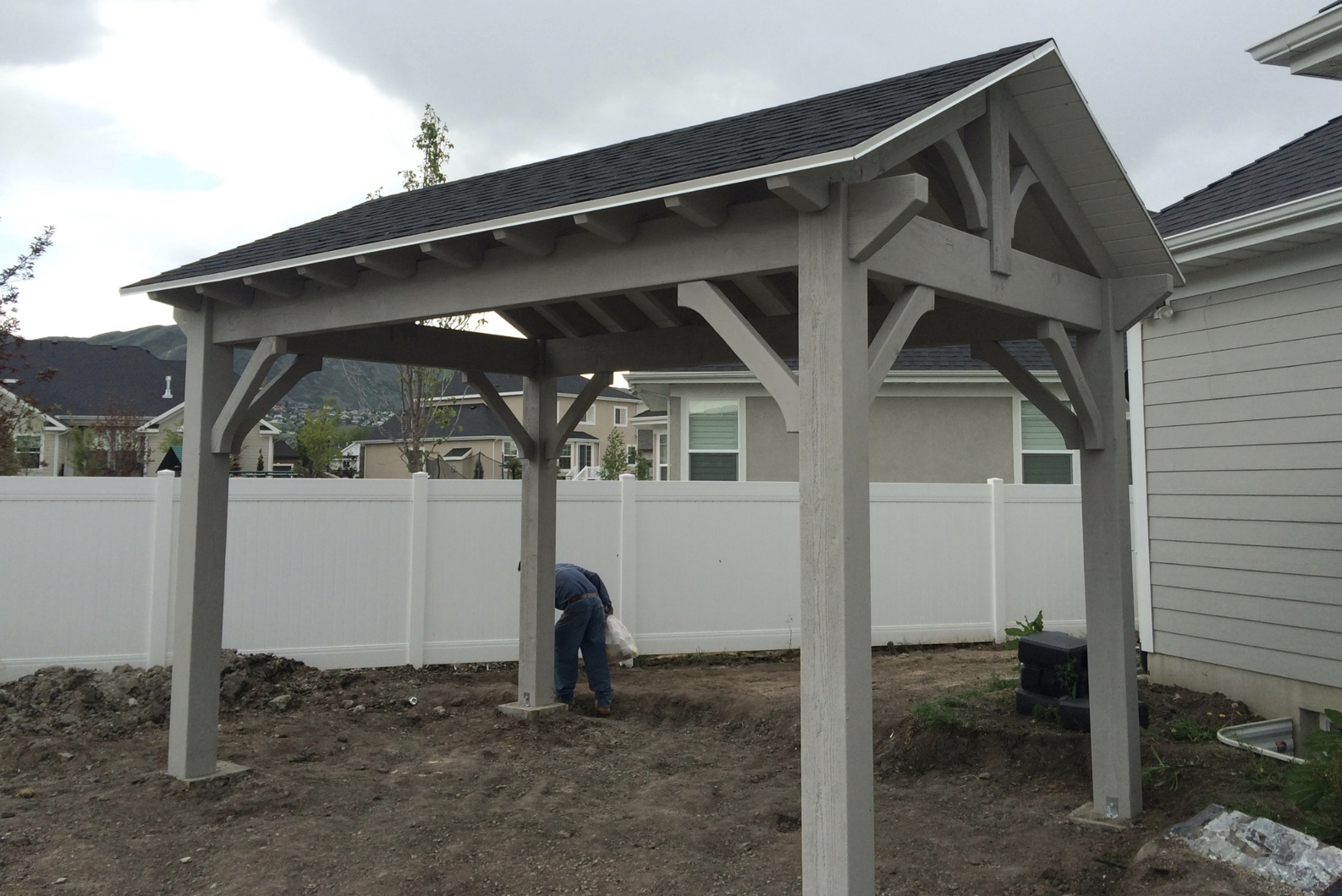 Backyard Pavilion Build: In-Progress Gable Frame Backyard pavilion under construction with gable roof; worker sets posts and anchors, illustrating how to build a pavilion