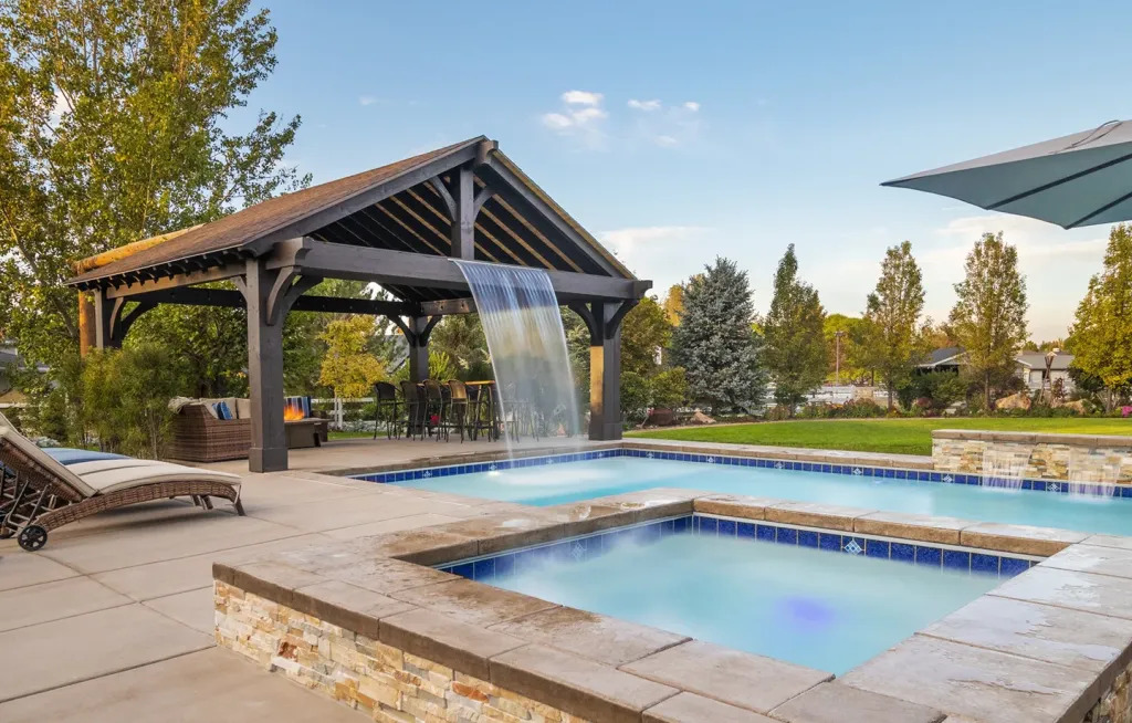 Custom timber frame pool pavilion with waterfall feature and outdoor seating in Murray, Utah.