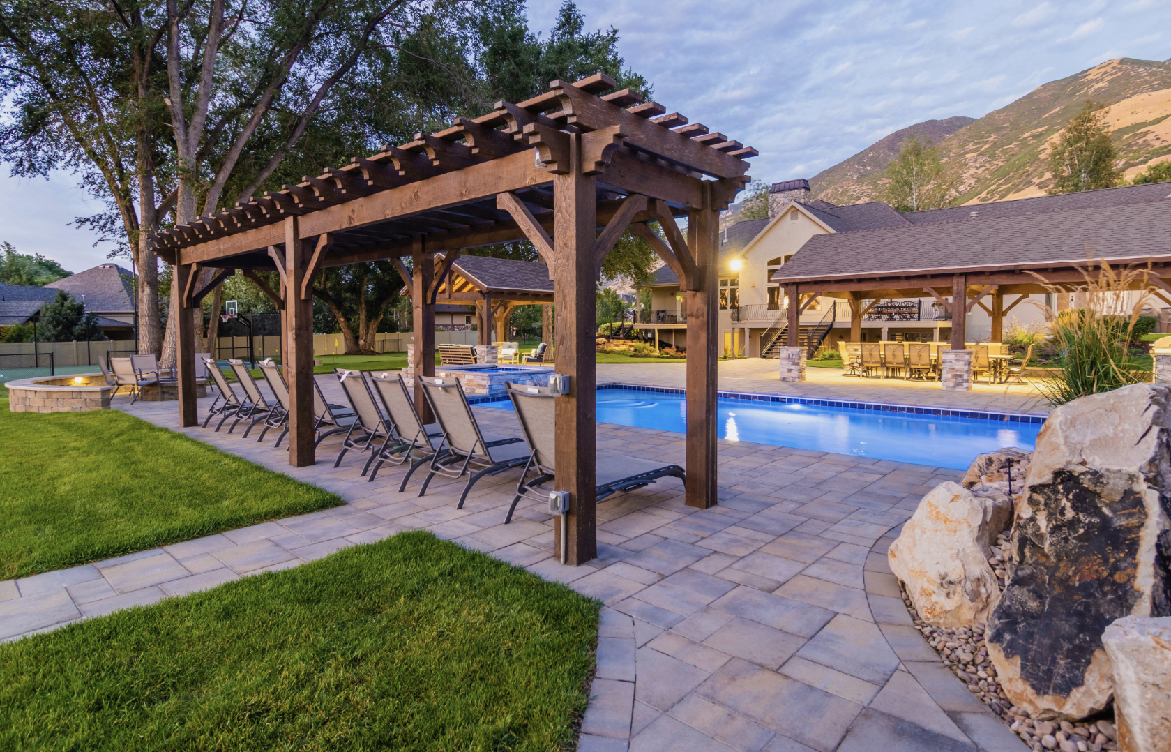 Timber Pergola by the Poolside Custom timber pergola beside a swimming pool, with lounge chairs and a stone fire pit, enhancing outdoor living space.