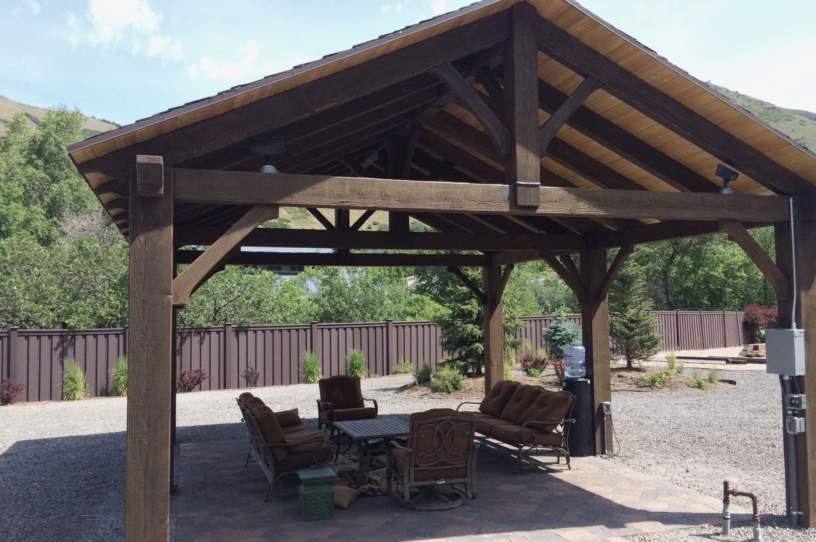 A dark timber frame pavilion with king post trusses and outdoor seating, built from durable wood using expert pavilion plans.