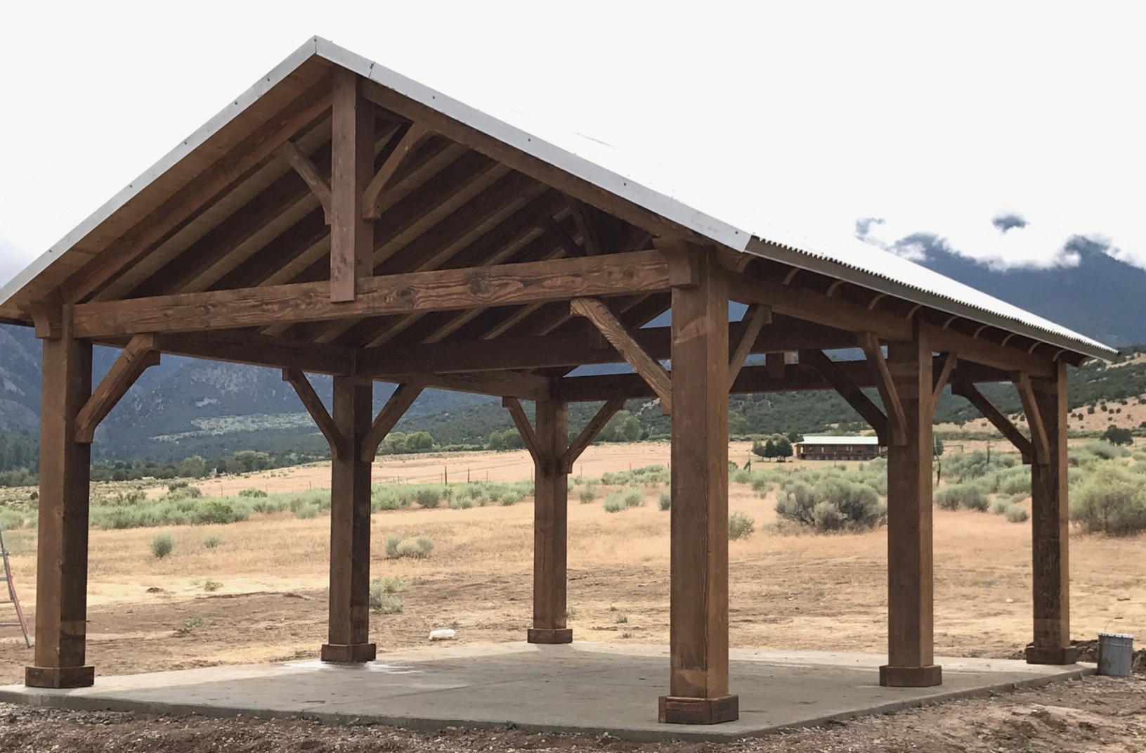 Rustic Timber Patio Pavilion Design A large wooden patio pavilion with a metal roof set against a scenic mountain backdrop, ideal for open-air gatherings and shade.