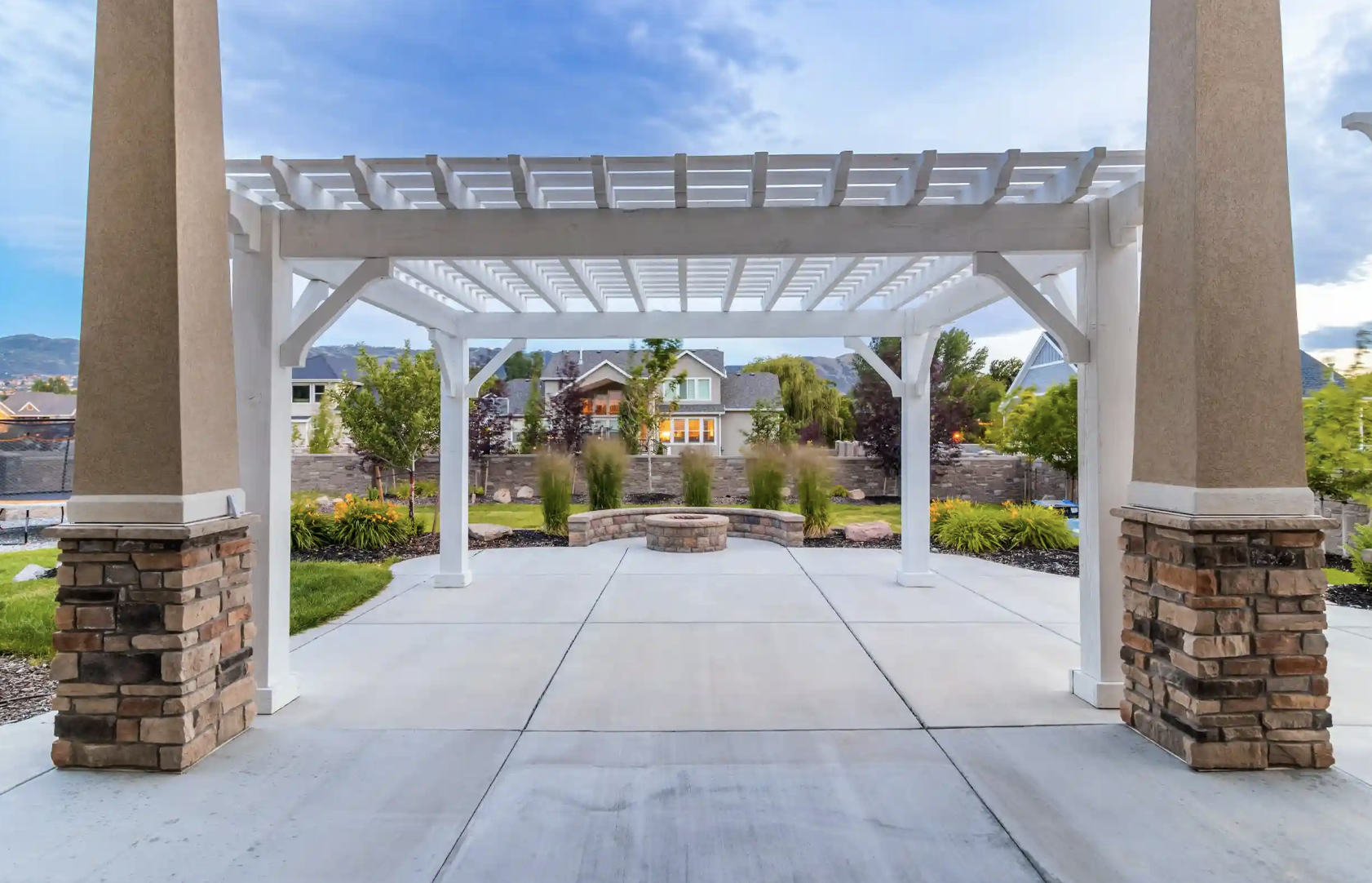 Custom White Timber Pergola by Wright Timberframe Elegant white timber pergola with stone column bases overlooking a landscaped backyard and fire pit, designed and built by Wright Timberframe.