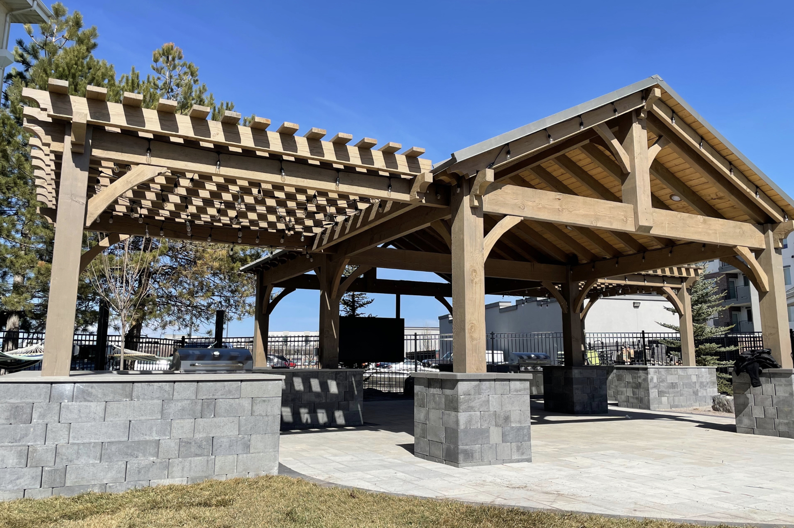 Timber Frame Pavilion with Pergola Large timber frame pavilion with attached pergola featuring stone bases, wooden beams, and outdoor grill setup for a modern backyard space.