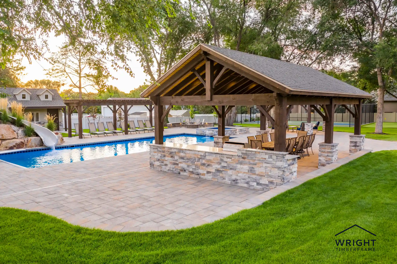 Timber pool pavilion with stone posts, outdoor dining, landscaped pool area with slide and lounge seating.