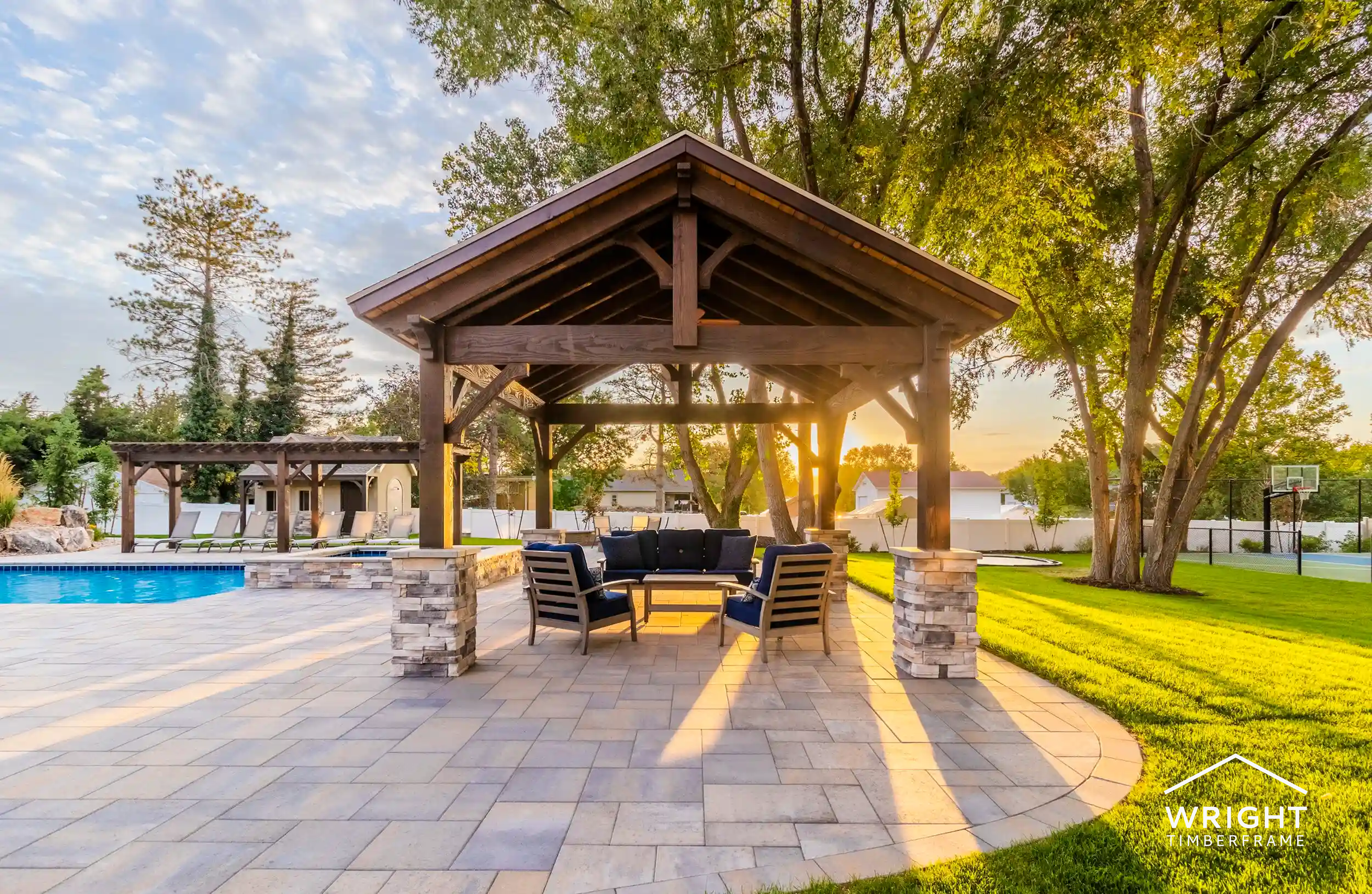 Timber Wood Outdoor Pavilion by Poolside Retreat Wood outdoor pavilion with timber beams and stone columns beside a pool, seating area, and landscaped backyard at sunset