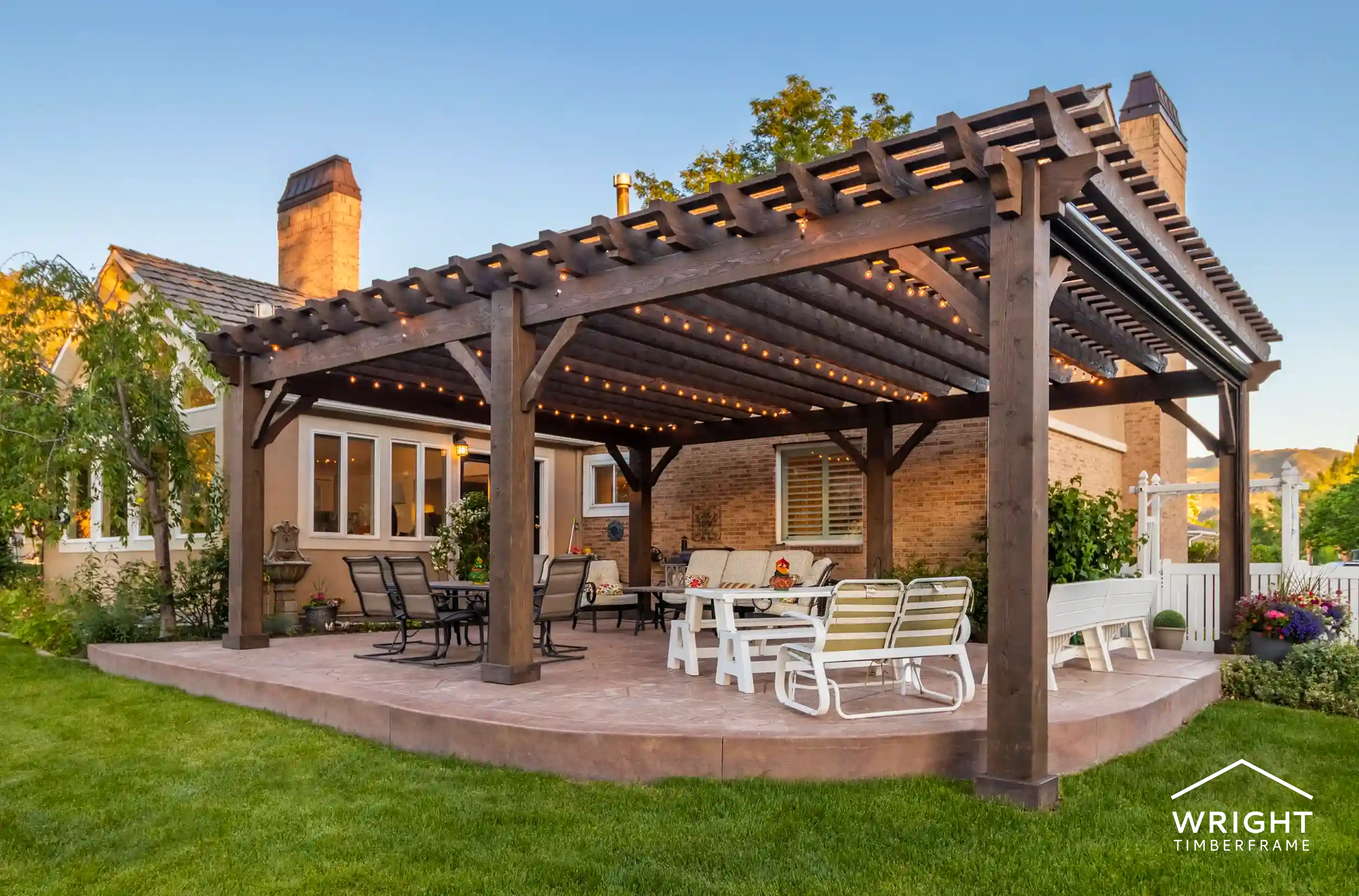 Custom Pergolas for Backyard Outdoor Living Spacious custom pergolas with timberframe beams and string lighting installed over a patio, creating a shaded outdoor living and seating area.
