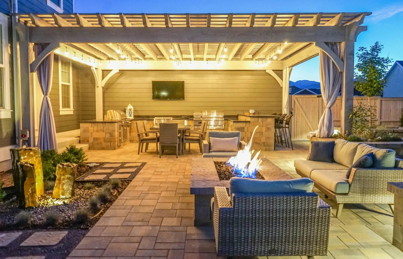 Timber frame patio with outdoor kitchen, fire pit, seating, and lighting, showcasing timber frame kit add-ons.
